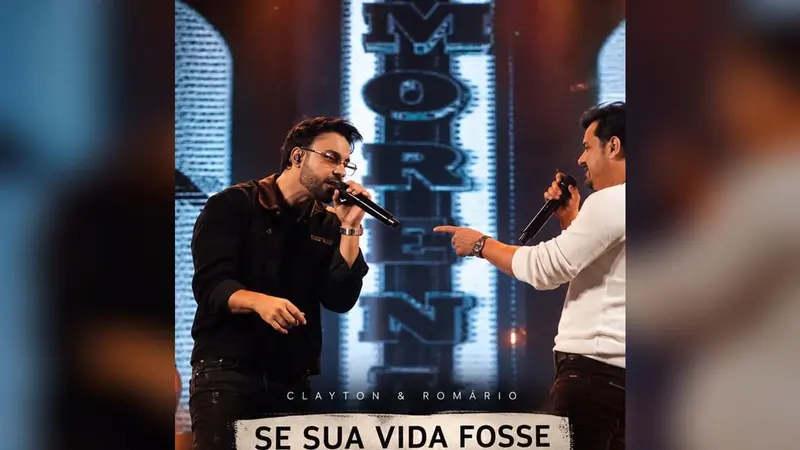 Os sertanejos Clayton e Romário, sorridentes, sentados lado a lado; um deles segura um violão