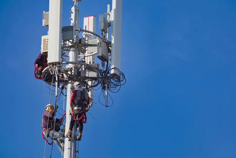 Técnicos com equipamento de segurança fazem manutenção no alto de uma torre de celular