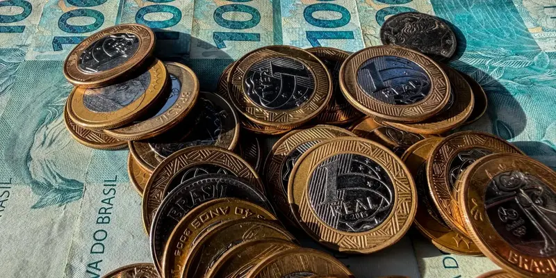 Moedas de um real empilhadas sobre cédulas de cem reais